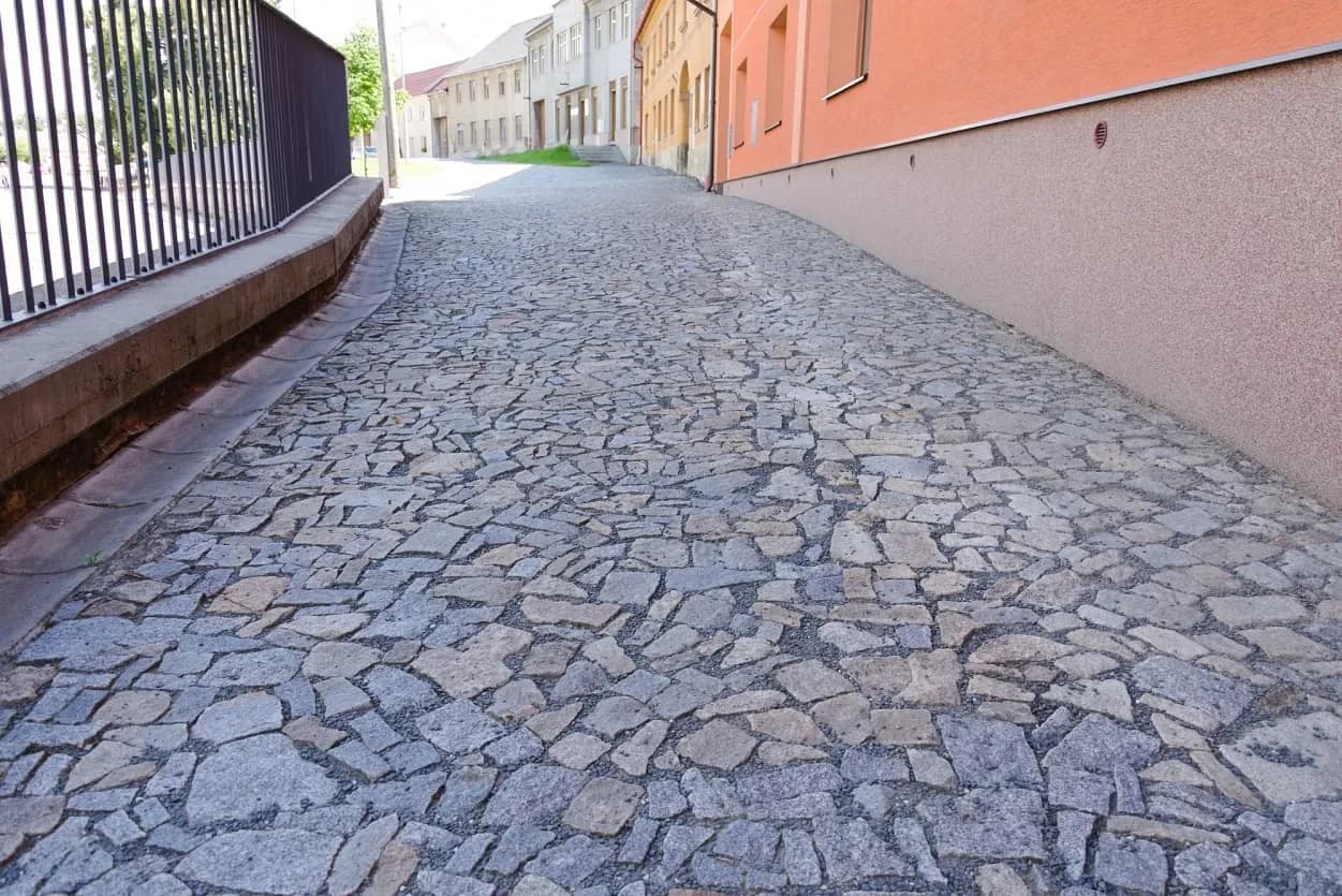Povrch dlážděný žulovými odštěpky v šedožlutém odstínu dodává ulici autentický vzhled a zároveň zajišťuje její životnost.