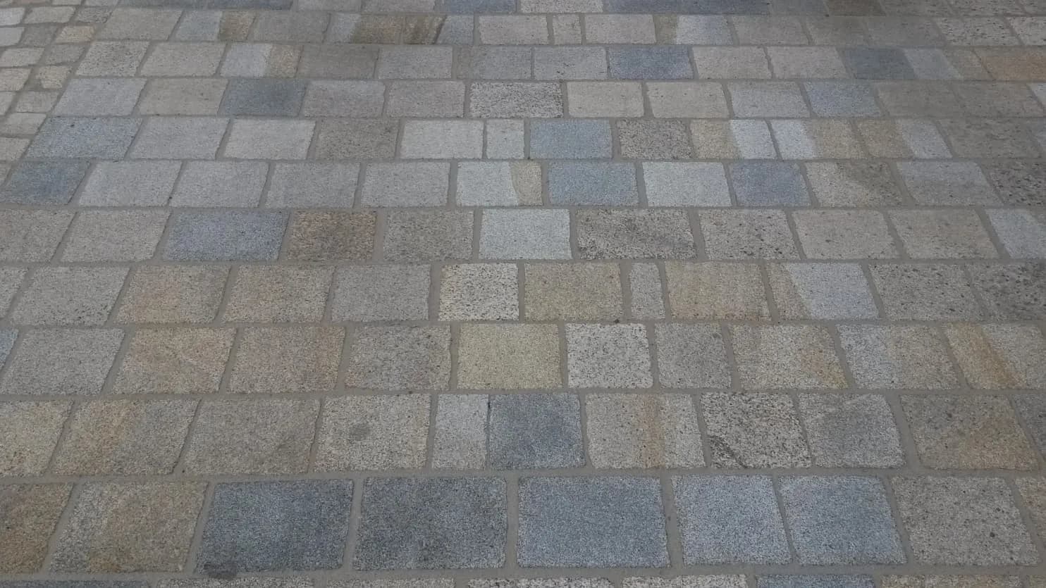 Dlažba z formátovaných žulových desek v různých odstínech, vytvářející odolný a estetický povrch.