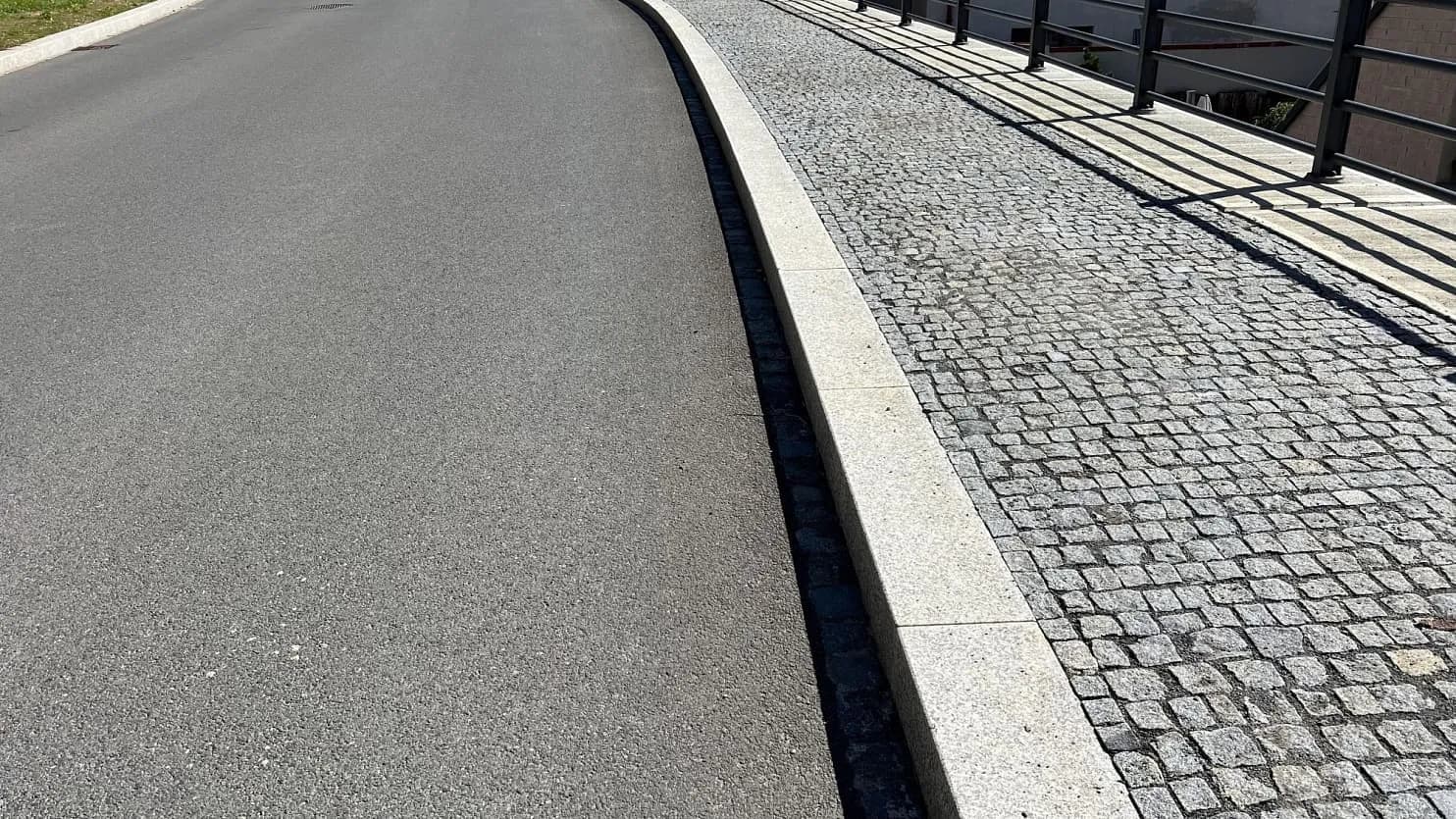 Chodník ze šedých žulových kostek, lemovaný řezaným obrubníkem, elegantně navazuje na asfaltovou vozovku.