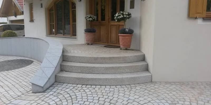 Elegantní vstupní schodiště z žuly s obloukovými stupni, žulovým obkladem zídky a dlažbou z formátovaných žulových kostek.