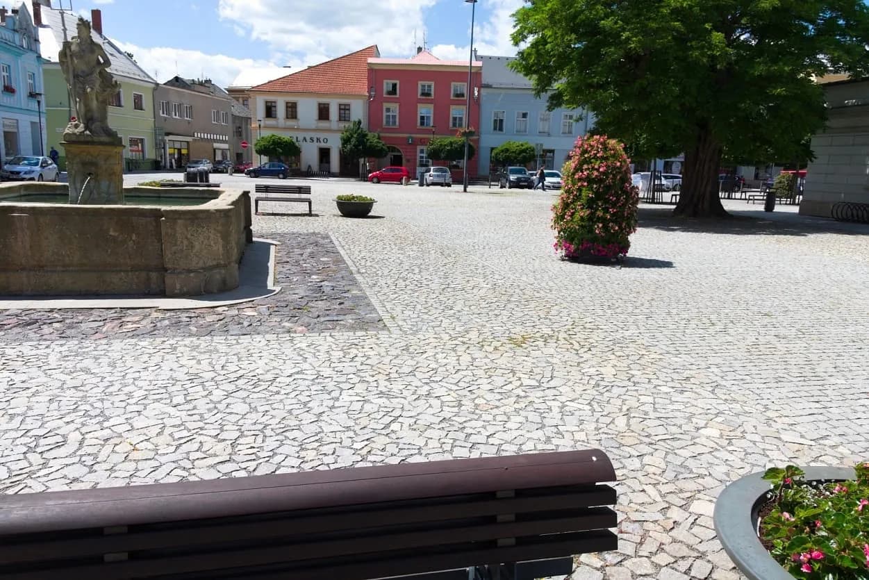 Historická kašna v Uničově s tříděnými žulovými odseky a květinovou výzdobou na dlážděném náměstí.