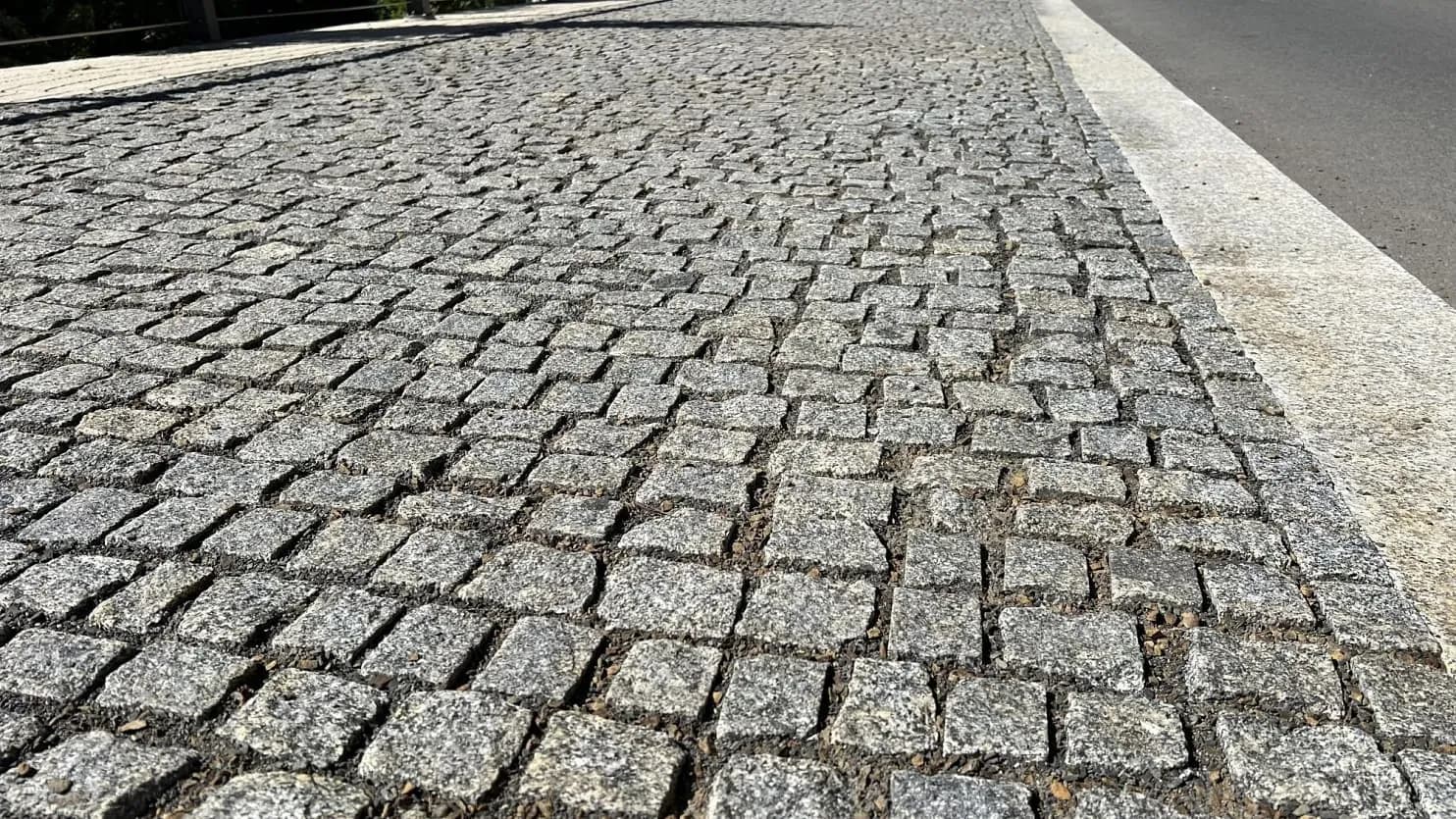 Detailní pohled na chodník z žulových kostek v šedém odstínu, precizně osazených vedle řezaného obrubníku pro odolnost a estetický vzhled.