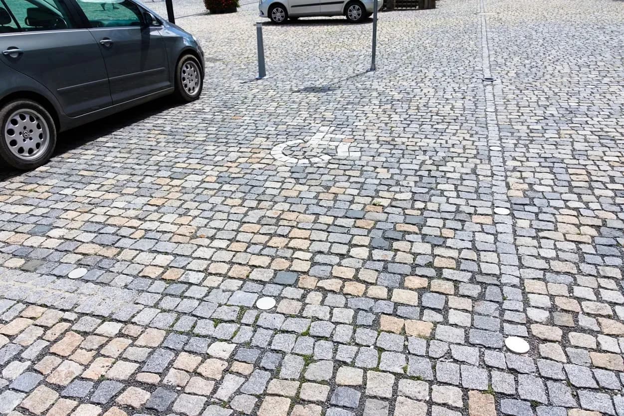 Parkovací místo pro invalidy na náměstí s dlažbou z přírodního kamene v různých odstínech.