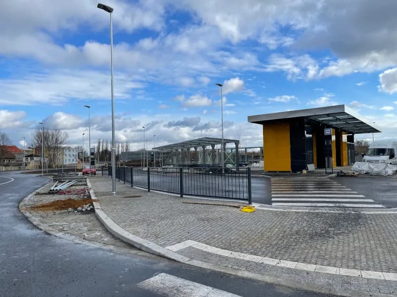 Autobusový terminál v Kralupech nad Vltavou během výstavby, s moderními přístřešky, žulovou dlažbou a veřejným osvětlením.