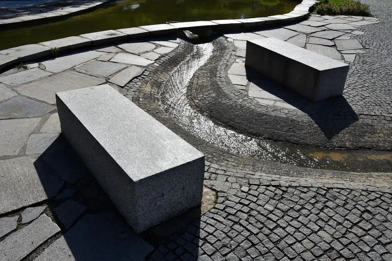 Žulové bloky sloužící jako lavičky u vodního prvku v Priessnitzových léčebných lázních, obklopené dlažbou z přírodního kamene