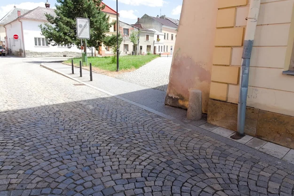 Žulová dlažba ve vějířovém vzoru, doplněná obrubníky a kamennými patníky v historické uličce Uničova.