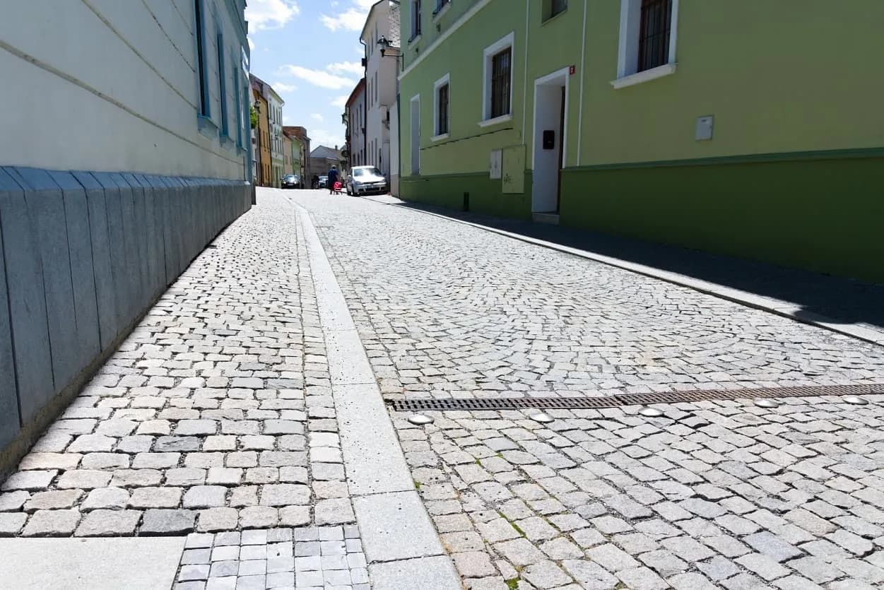 Mírně svažitá ulice v Uničově s žulovými kostkami a obrubníky, zdůrazňující historický ráz města.