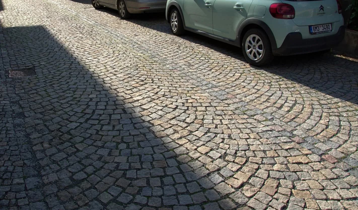 Žulová dlažba v obloukovém vzoru na ulici s parkujícími auty, kombinující šedé a žluté tóny pro estetický a trvanlivý povrch.